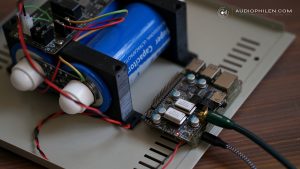 Raspberry Pi mit aufgestecktem Transport-HAT auf einer Gehaeusegrundplatte, links die Supercap-Stromversorgung mit blauen Ultrakondensatoren, verbunden ueber farbige Litzen